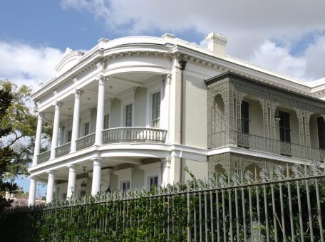 A White house is fenced behind a beautiful wall of greenery.